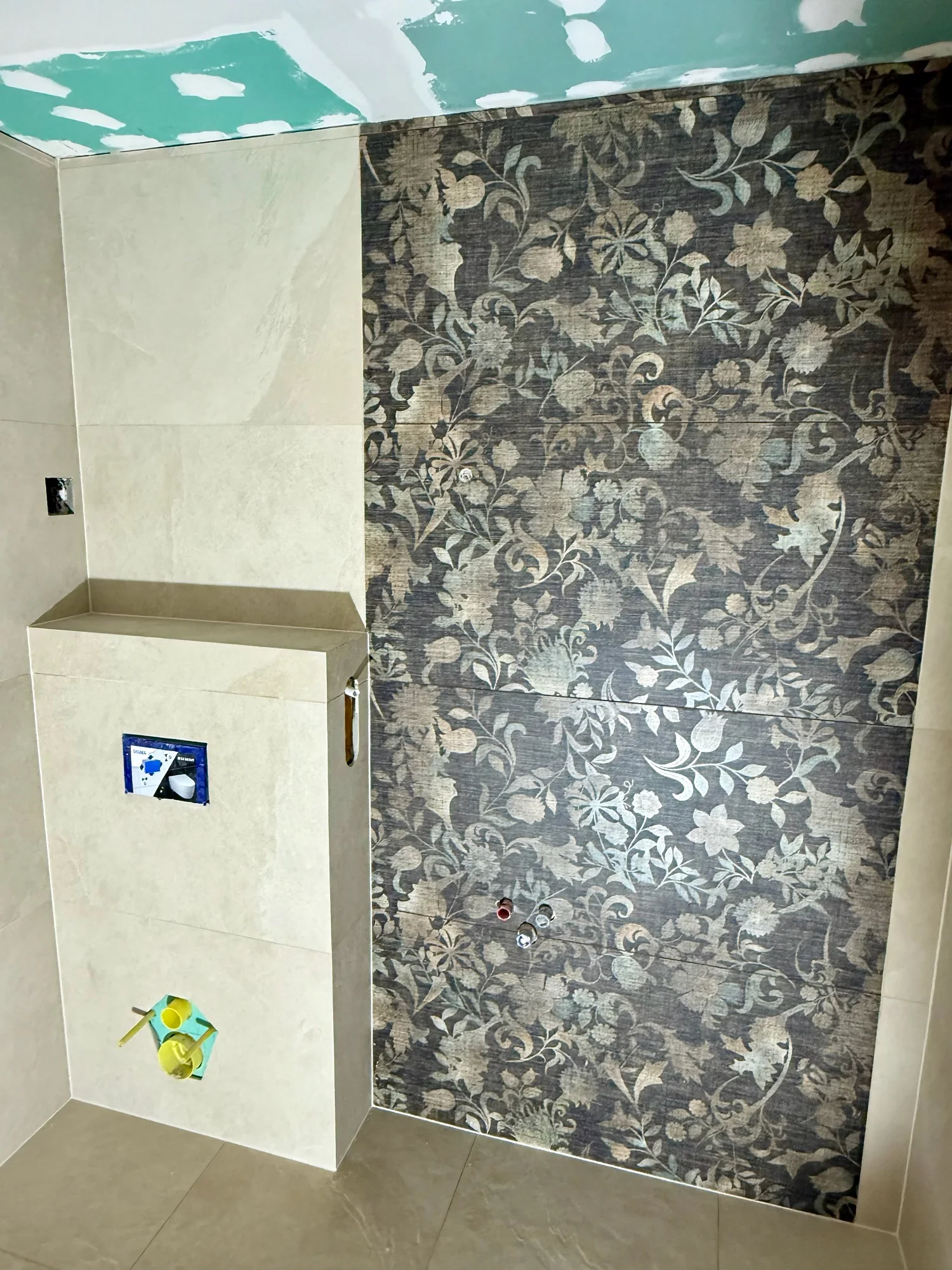 Patterned wall tiles and a tiled toilet cistern wall during installation.